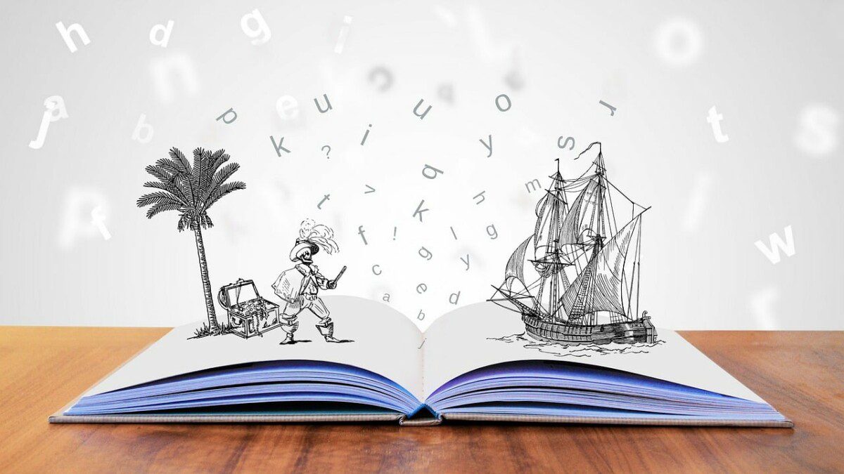 Das Foto zeigt ein aufgeschlagenes Buch, welches auf einem braunen Tisch liegt. Man sieht das Buch von der Frontalansicht. Auf der rechten Seite des Buches ist ein Piratenschiff im Bleistift-Comicstil zu sehen und auf der linken ein Pirat auf einer Insel. Hinter dem Piraten steht eine Palme und es liegt ein Schatz. Der Hintergrund des Bildes ist weiß und sind Buchstaben in beistiftschrift zu sehen. 