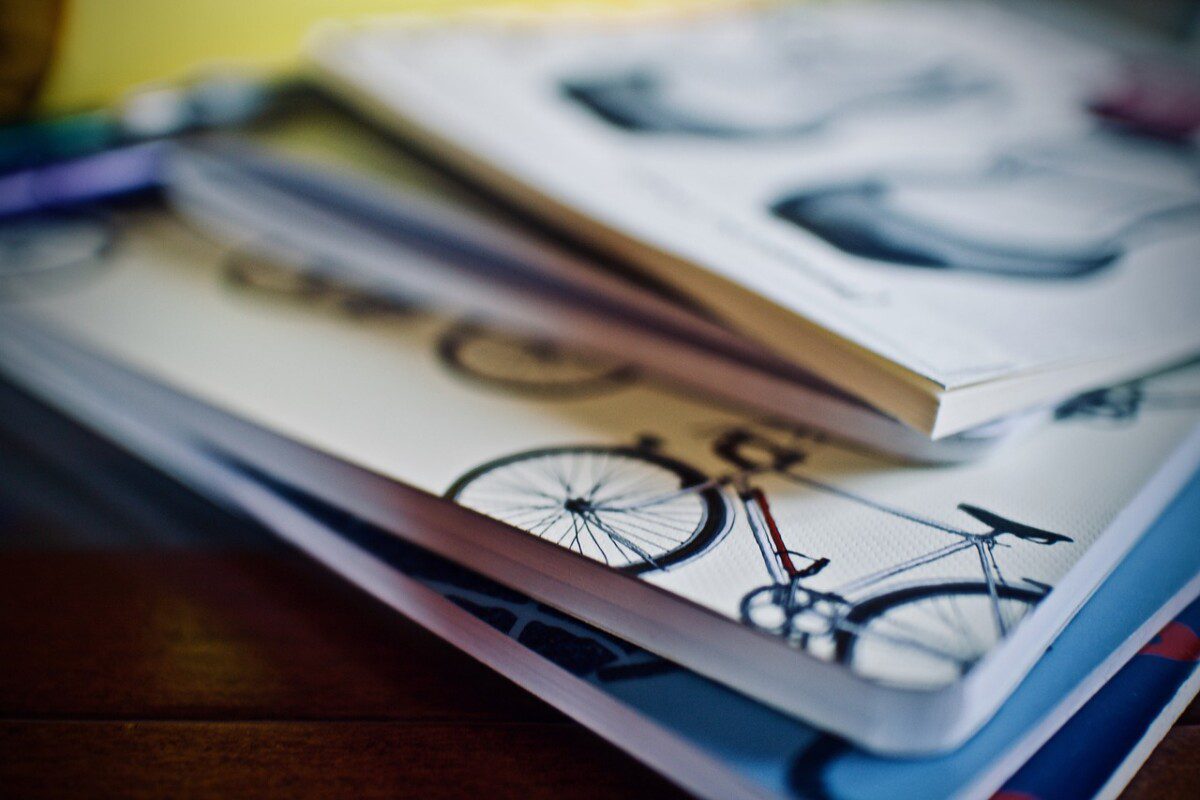 Das Foto zeigt einen Haufen von Heften. Auf dem letzten Heft sieht man ein rotes Fahrrad.