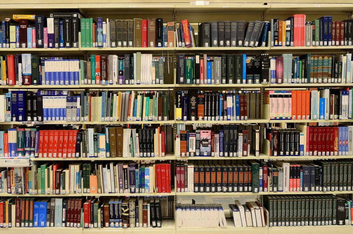 Das Bild zeigt eine Universitätsbibliothek. Man sieht dabei ein Bücherregal, welches neben Bücher auch Forschungsergebnisse und Mappen enthält. 