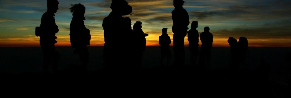 Das Foto zeigt Silhouetten während eines Sonnenuntergangs, der Nachthimmel ist dabei schon dunkel gefärbt und man sieht nur die Umrisse der Personen.- Es steht symbolisch für unser Team und den DeinText.at „Über Uns“ Bereich.
