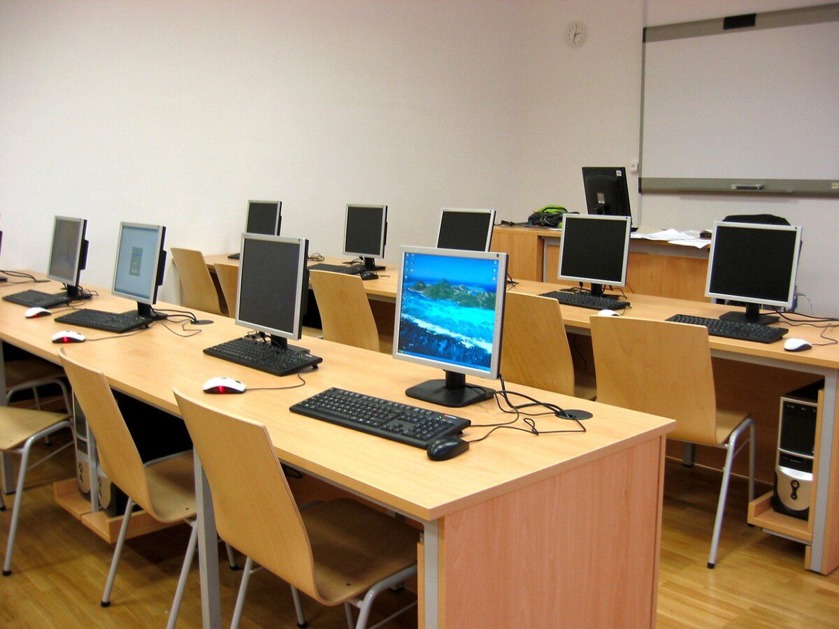Das Fotozeigt eine Unterrichtsraum der Tische auf denen Computer stehen darstellt. Es sind drei Reihen von Tischen zu sehen. 