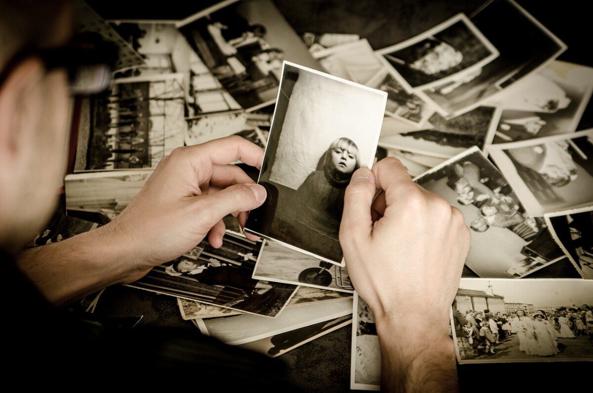 Auf dem schwarzweis Foto sieht man Hände, die für die Biografie-Arbeit alte Bilder durchgehen. Die Hände halten gerade eins der Fotos hoch, das ein junges Mädchen zeigt.